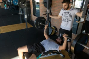 : A man dong barbell next to his trainer